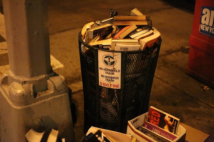 A city trash bin full of books.