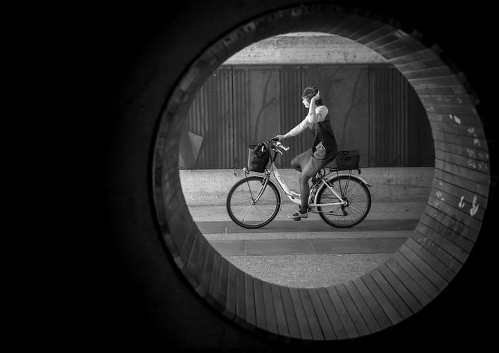 A black and white photograph of a woman on a bicycle, as seen through a circular window.