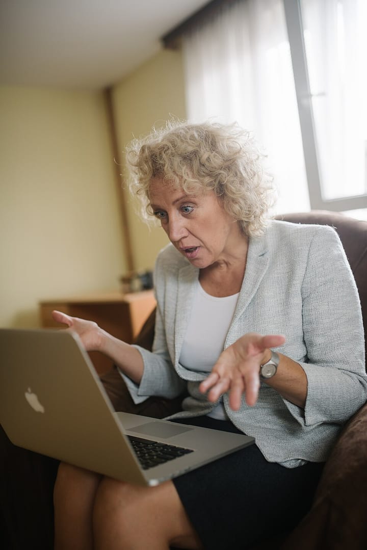 White woman looking confused while sitting in an armchair with a laptop in her lap