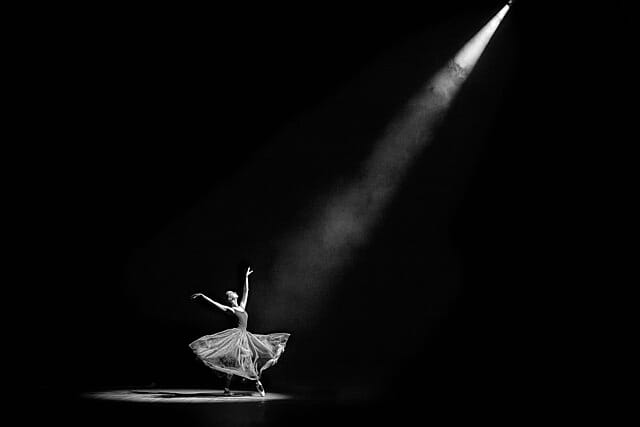 A ballerina in a spotlight, alone on a dark stage.